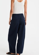 A woman shown from the back wearing a white ribbed knit tank top and navy wide-leg trousers, standing against a plain light grey studio background.