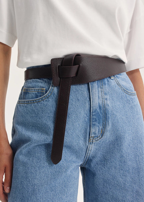 Person wearing a brown belt with blue jeans on a plain background