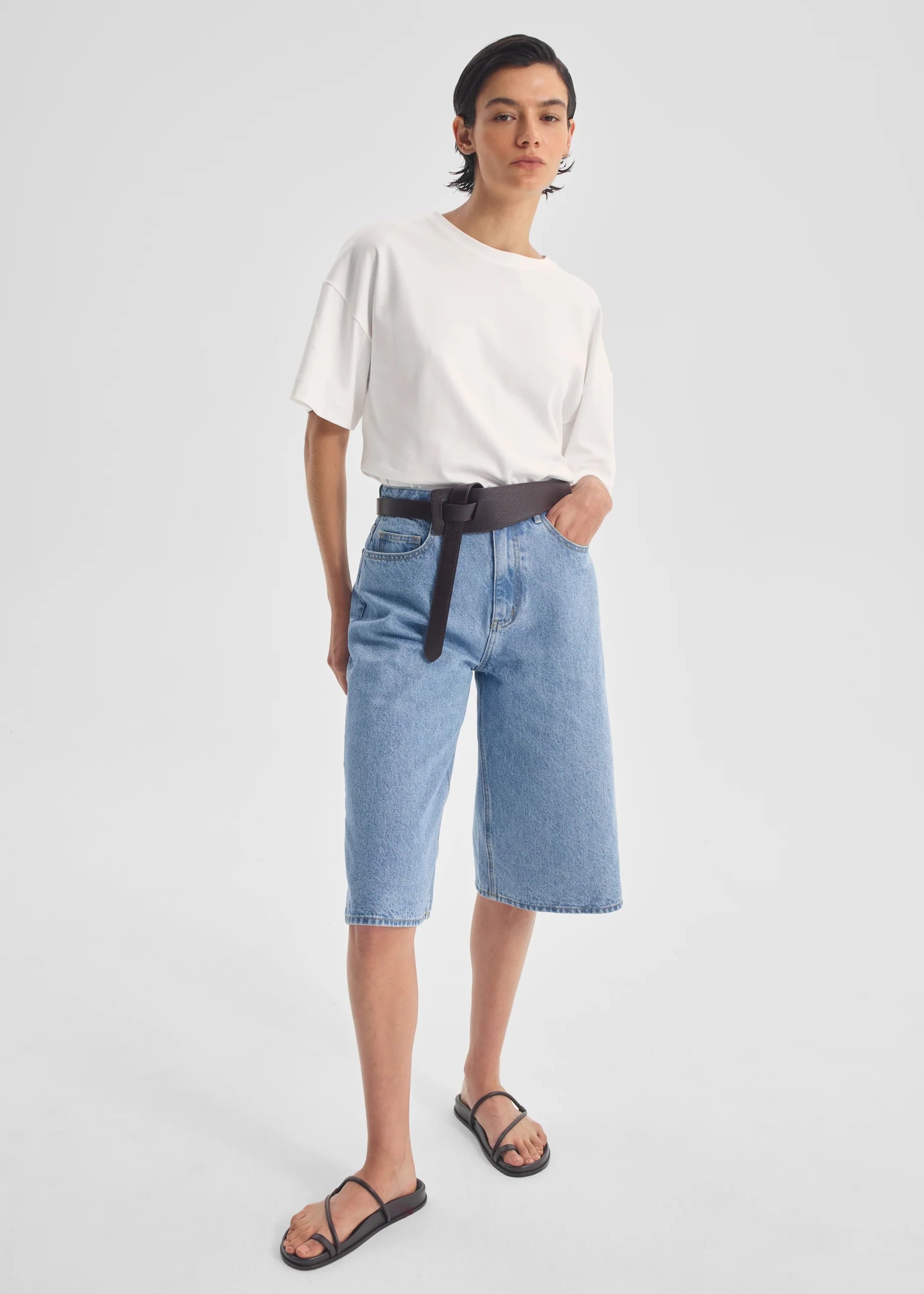Person wearing a white top and blue denim shorts on a plain background