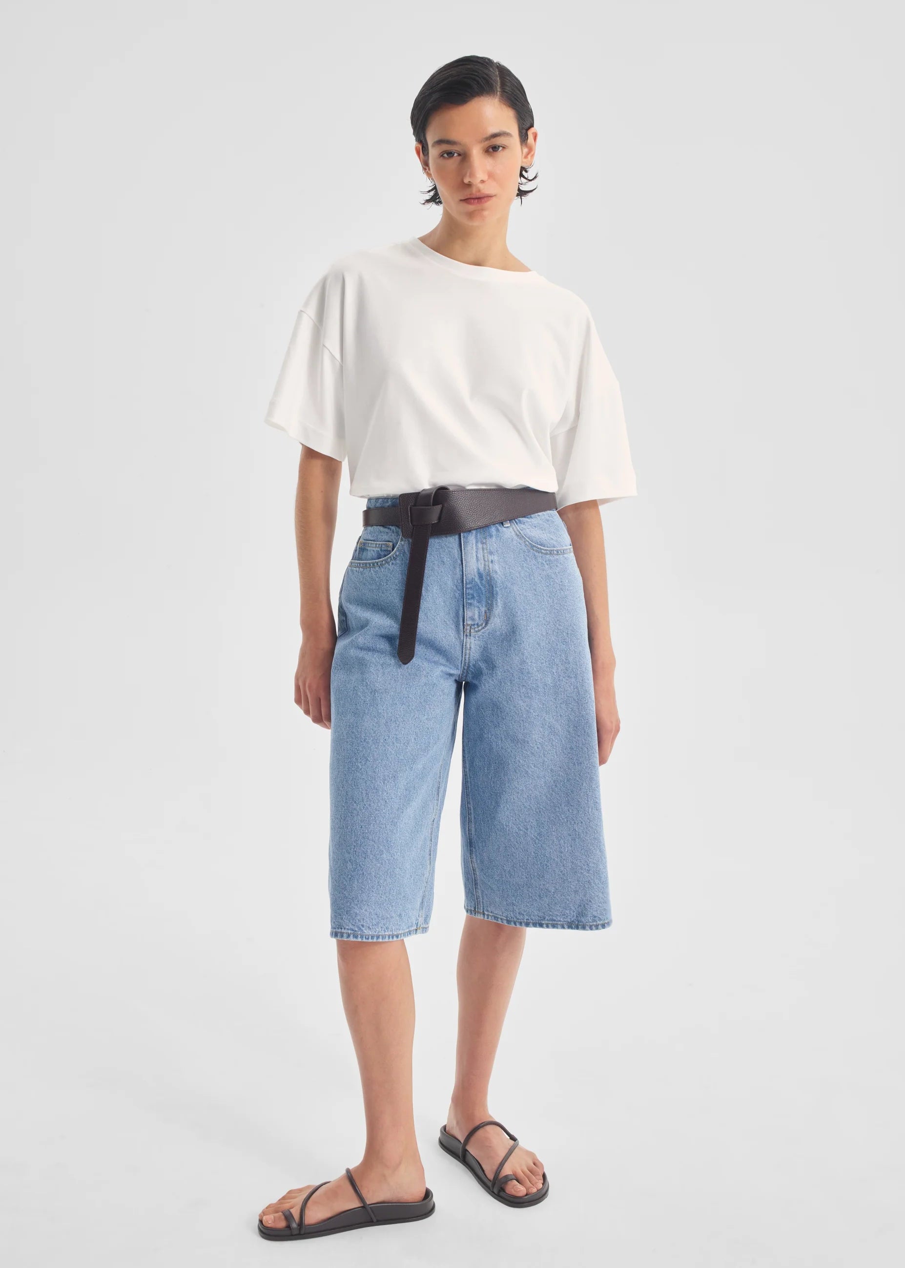 Person wearing a white top and blue denim shorts on a light gray background