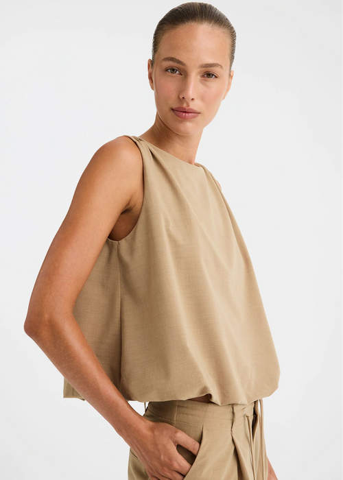 A woman modelling a sleeveless beige top and matching beige pants against a clean white studio background.