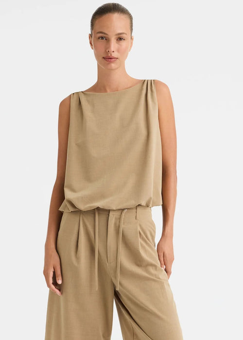 A woman modelling a sleeveless beige top and matching beige pants against a clean white studio background.