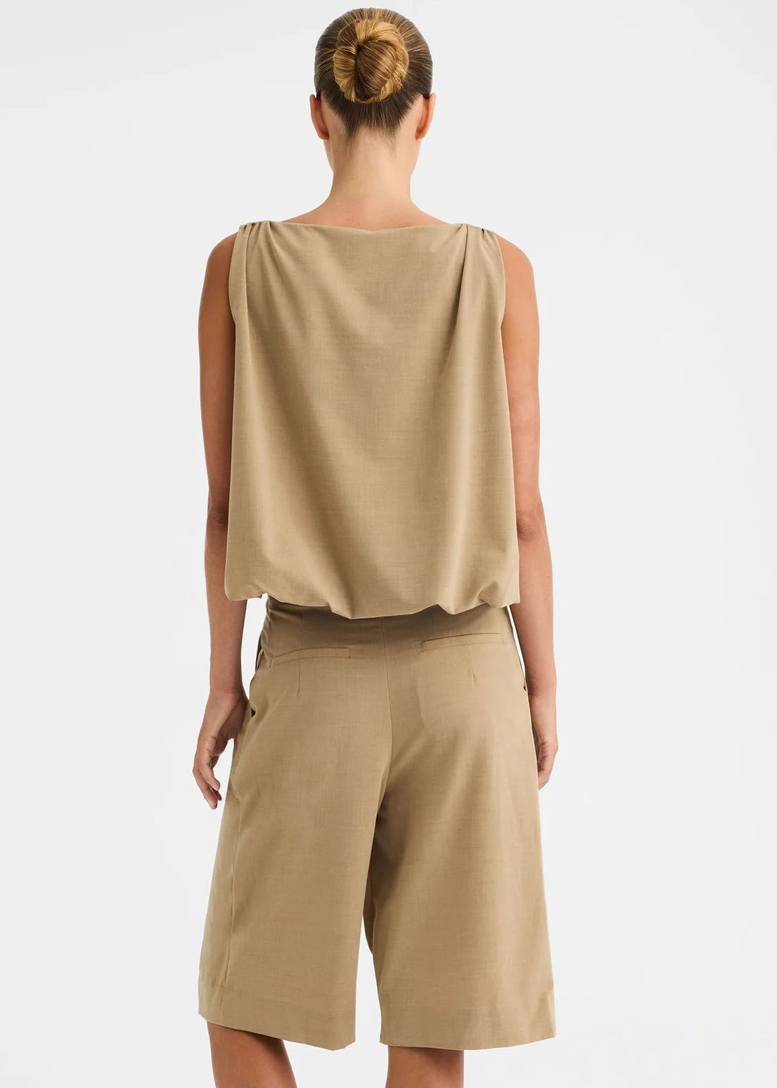 A woman modelling a sleeveless beige top and matching beige pants against a clean white studio background.