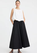 A woman modelling a sleeveless white top with a high neckline and black skirt against a light grey studio background.