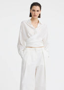 A model wearing a white long-sleeve button-up shirt and matching white wide-leg trousers, styled with black flip-flop sandals against a plain white studio background.