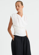 A woman modelling a white sleeveless wrap-style top paired with black wide-leg pants against a clean white studio background.