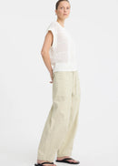 A woman stands against a plain white studio background wearing a white long-sleeve knit top with subtle horizontal texture details, beige wide-leg drawstring pants, and black sandals.