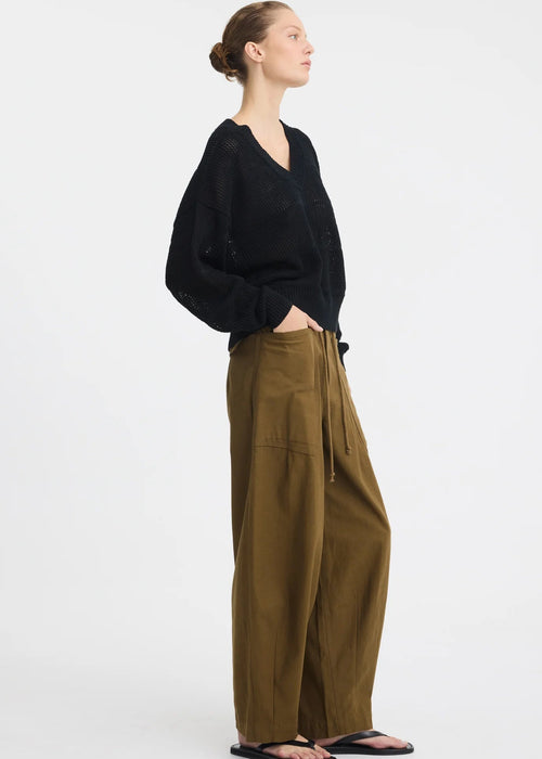 A model wearing a black sleeveless knit top and olive green wide-leg pants with a drawstring waist, paired with black sandals, against a plain white studio background.