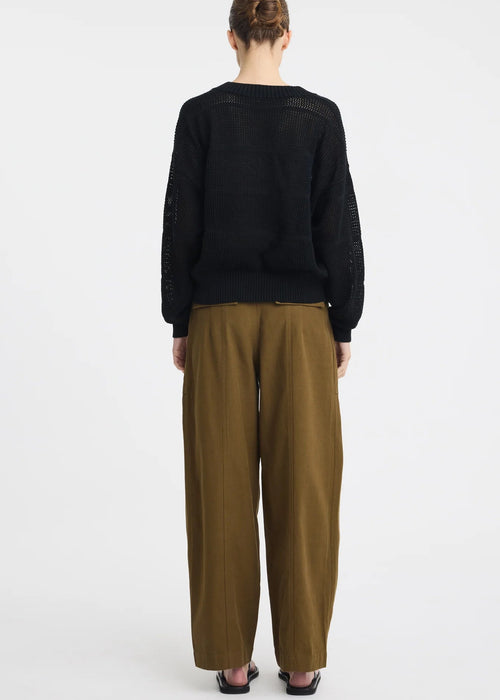A model wearing a black sleeveless knit top and olive green wide-leg pants with a drawstring waist, paired with black sandals, against a plain white studio background.