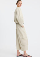 A model wearing a light beige two-piece outfit consisting of a cropped long-sleeve top and matching wide-leg cargo pants, paired with black flip-flop sandals, against a plain white studio background.
