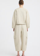 A model wearing a light beige two-piece outfit consisting of a cropped long-sleeve top and matching wide-leg cargo pants, paired with black flip-flop sandals, against a plain white studio background.