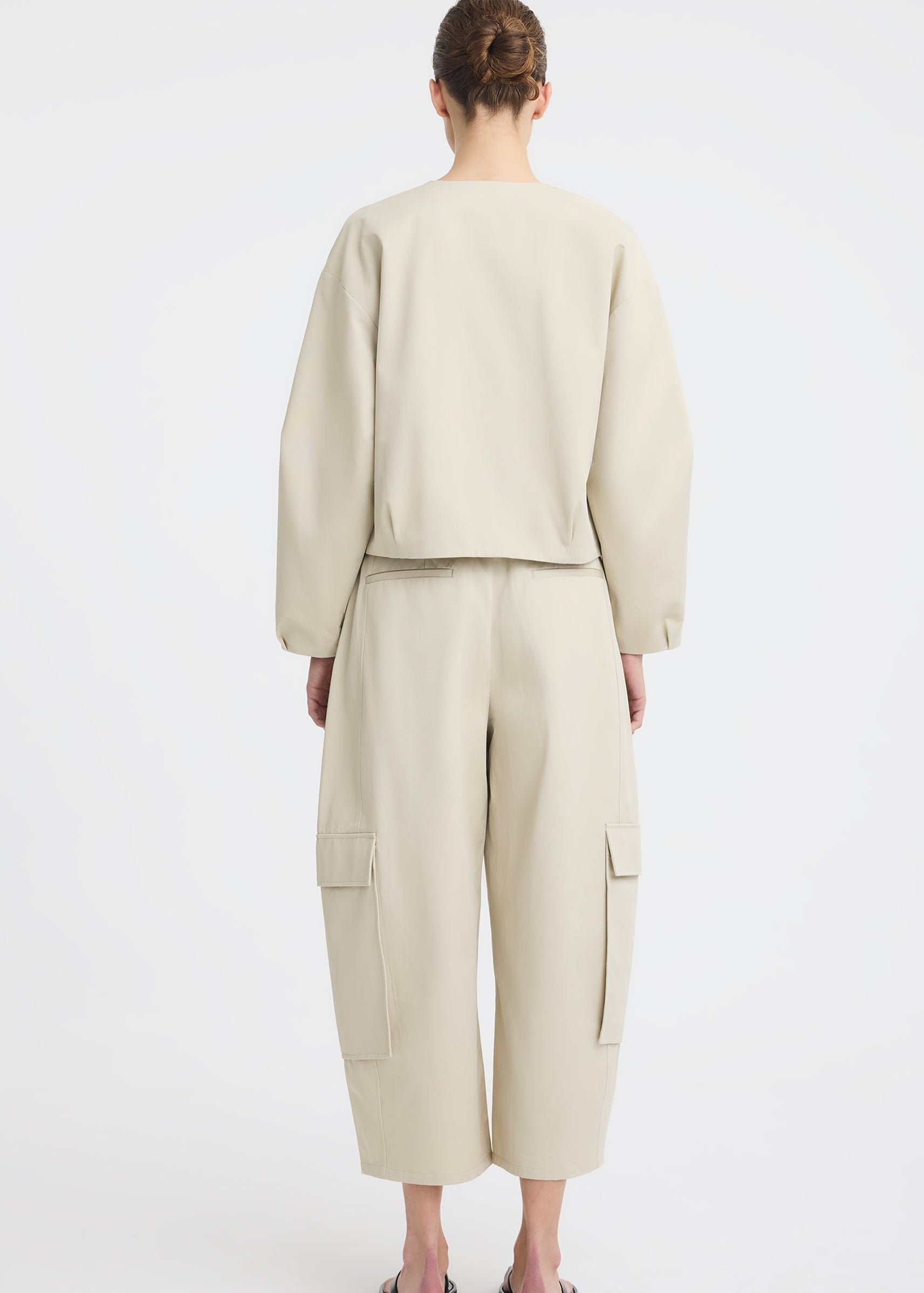 A model wearing a light beige two-piece outfit consisting of a cropped long-sleeve top and matching wide-leg cargo pants, paired with black flip-flop sandals, against a plain white studio background.