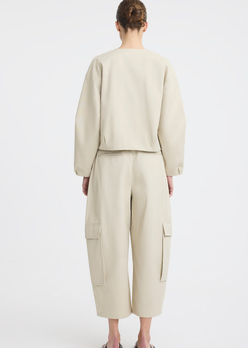 A model wearing a light beige two-piece outfit consisting of a cropped long-sleeve top and matching wide-leg cargo pants, paired with black flip-flop sandals, against a plain white studio background.