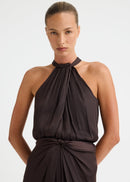 A woman modelling a dark brown halter-neck top with a gathered, draped bodice and a matching draped skirt, set against a plain light grey studio background.
