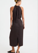 A woman modelling a dark brown halter-neck midi dress from the back, featuring a tie-neck detail and a side slit, set against a plain white studio background.