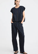 A model stands against a light grey studio background wearing a dark navy sleeveless top with a front zipper and matching dark navy wide-leg pants with large front pockets.
