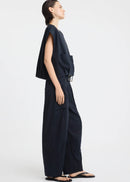A model stands against a light grey studio background wearing a dark navy sleeveless top with a front zipper and matching dark navy wide-leg pants with large front pockets.