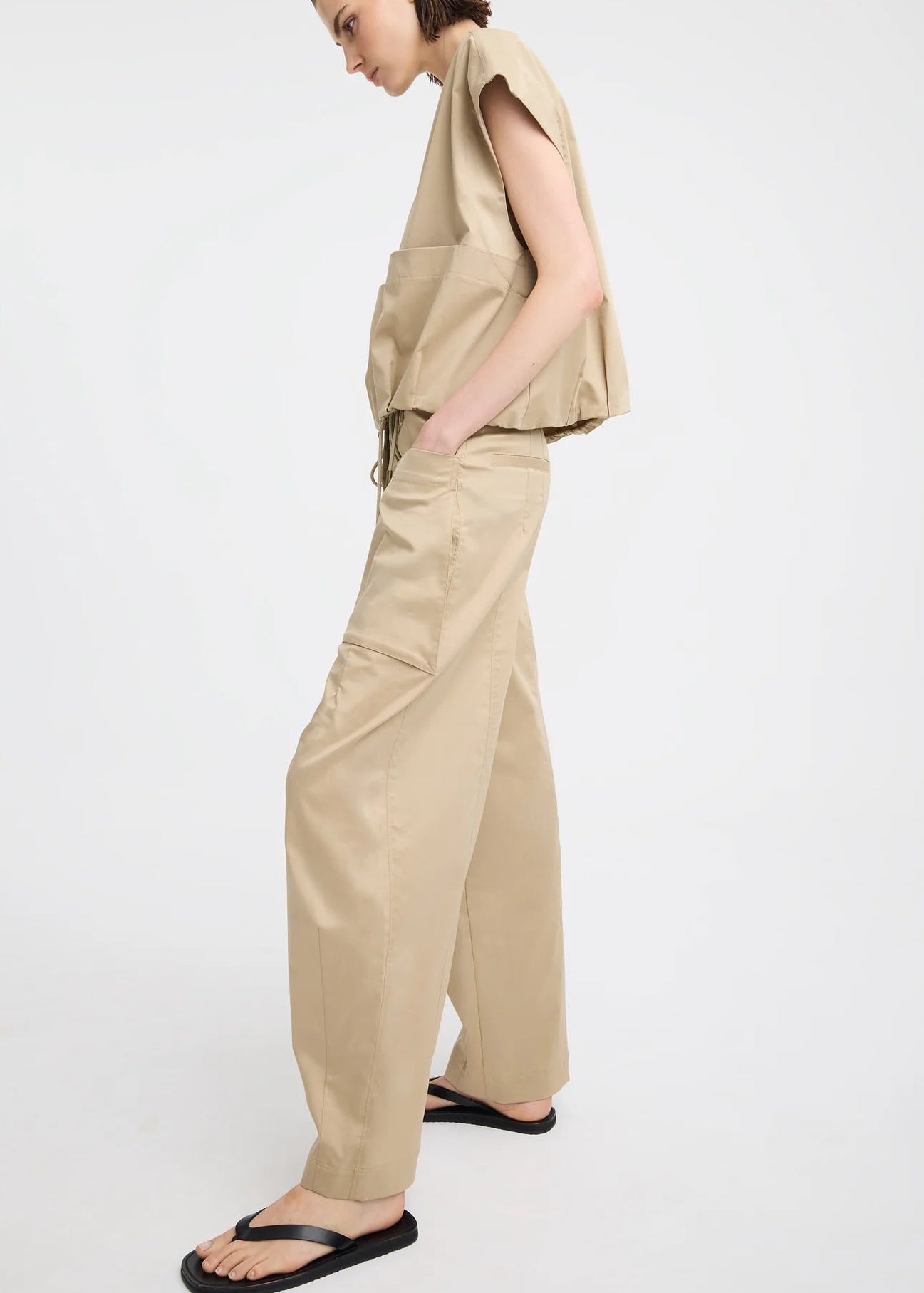 A model wearing a beige sleeveless top and matching wide-leg cargo pants, paired with black flip-flop sandals, photographed against a plain white studio background.