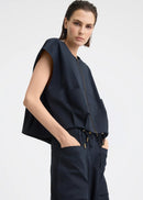A model wearing a dark navy blue sleeveless top with a front zipper and matching dark pants, photographed against a light grey studio background.