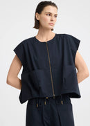 A model wearing a dark navy blue sleeveless top with a front zipper and matching dark pants, photographed against a light grey studio background.
