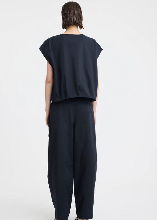 A model wearing a dark navy blue sleeveless top with a front zipper and matching dark pants, photographed against a light grey studio background.
