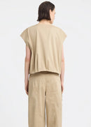 A model wearing a beige sleeveless utility vest with a front zipper and large front pockets, paired with matching beige pants, against a light grey studio background.