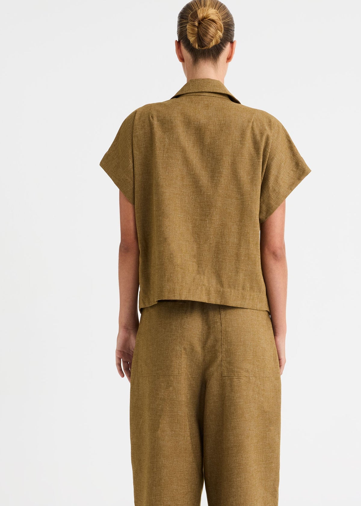 A model wearing a matching olive-brown linen two-piece set featuring a belted wrap-style top and wide-leg trousers, shot against a plain light grey studio background.