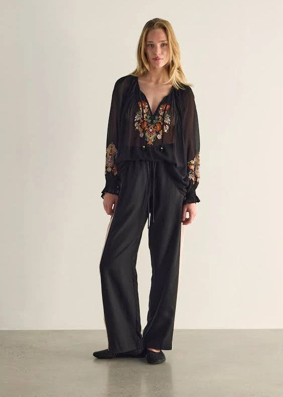 Woman wearing a black blouse with floral embroidery and black pants on a plain background