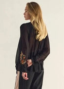 Woman wearing a black blouse with floral embroidery on a beige background