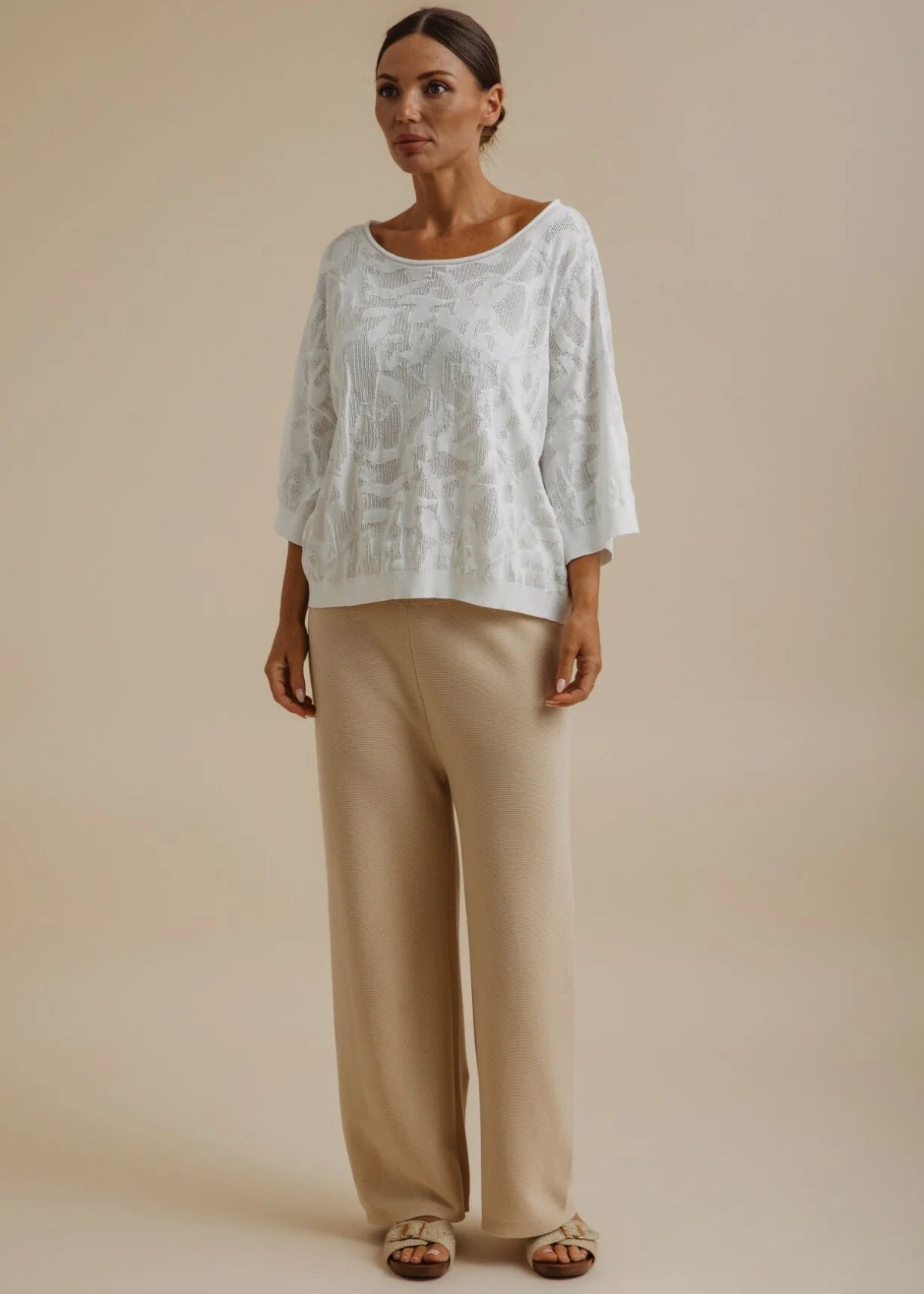 Woman wearing a white lace top and beige pants against a beige background