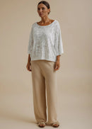 Woman wearing a white lace top and beige pants against a beige background