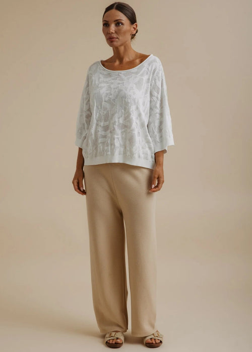 Woman wearing a white lace top and beige pants against a beige background