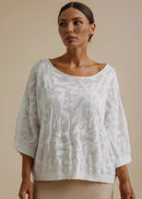 Woman wearing a white lace top and beige pants against a beige background
