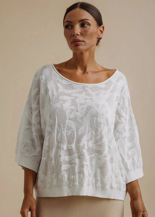 Woman wearing a white lace top and beige pants against a beige background