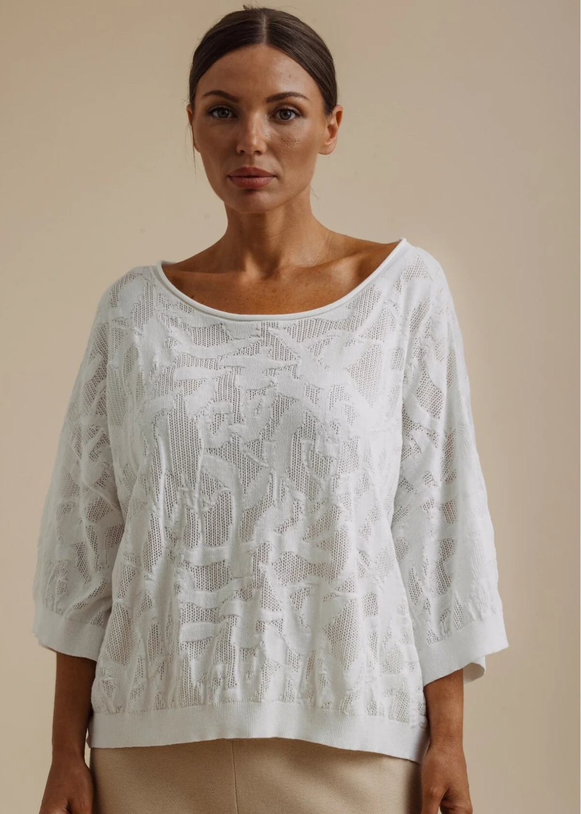Woman wearing a white lace top and beige pants against a beige background