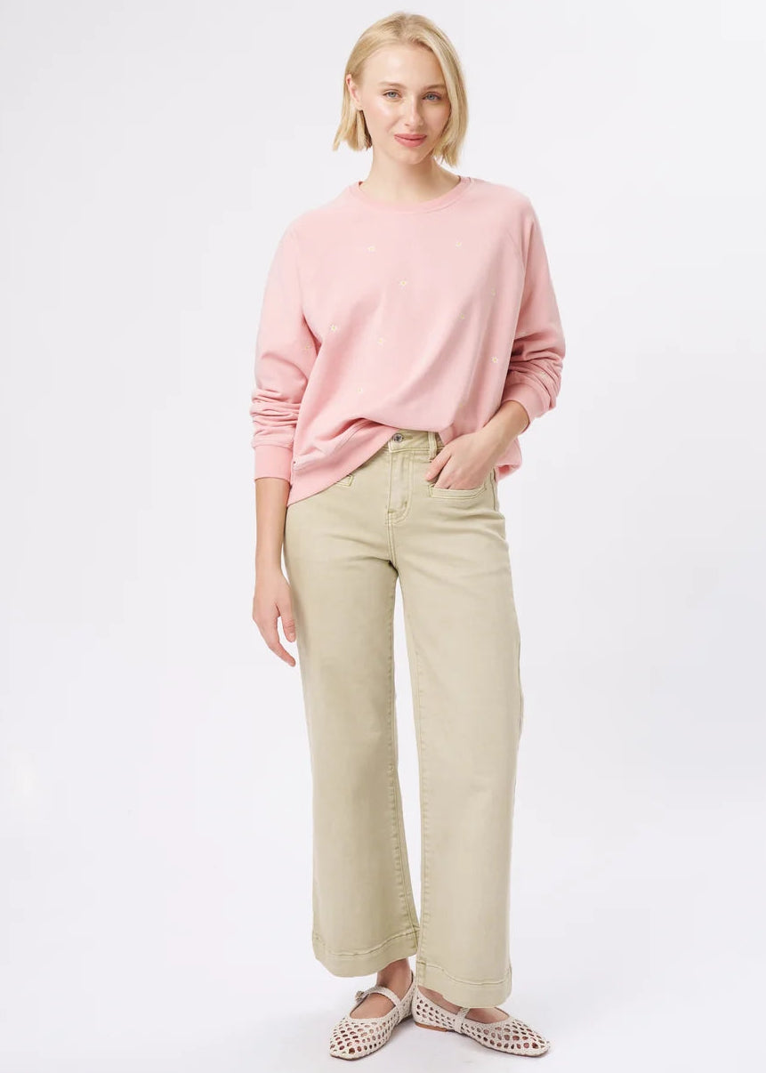 A woman modelling a light pink long-sleeve crewneck sweatshirt and beige wide-leg cropped pants, paired with patterned flat shoes, against a plain white studio background.