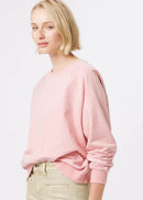 A woman modelling a light pink long-sleeve crewneck sweatshirt and beige wide-leg cropped pants, paired with patterned flat shoes, against a plain white studio background.