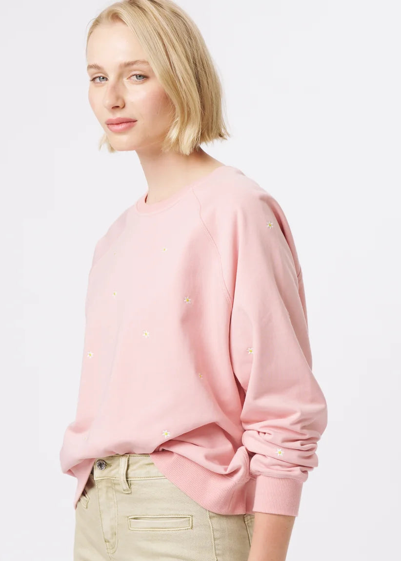 A woman modelling a light pink long-sleeve crewneck sweatshirt and beige wide-leg cropped pants, paired with patterned flat shoes, against a plain white studio background.