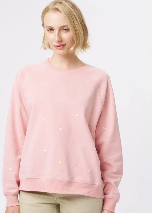 A woman modelling a light pink long-sleeve crewneck sweatshirt and beige wide-leg cropped pants, paired with patterned flat shoes, against a plain white studio background.