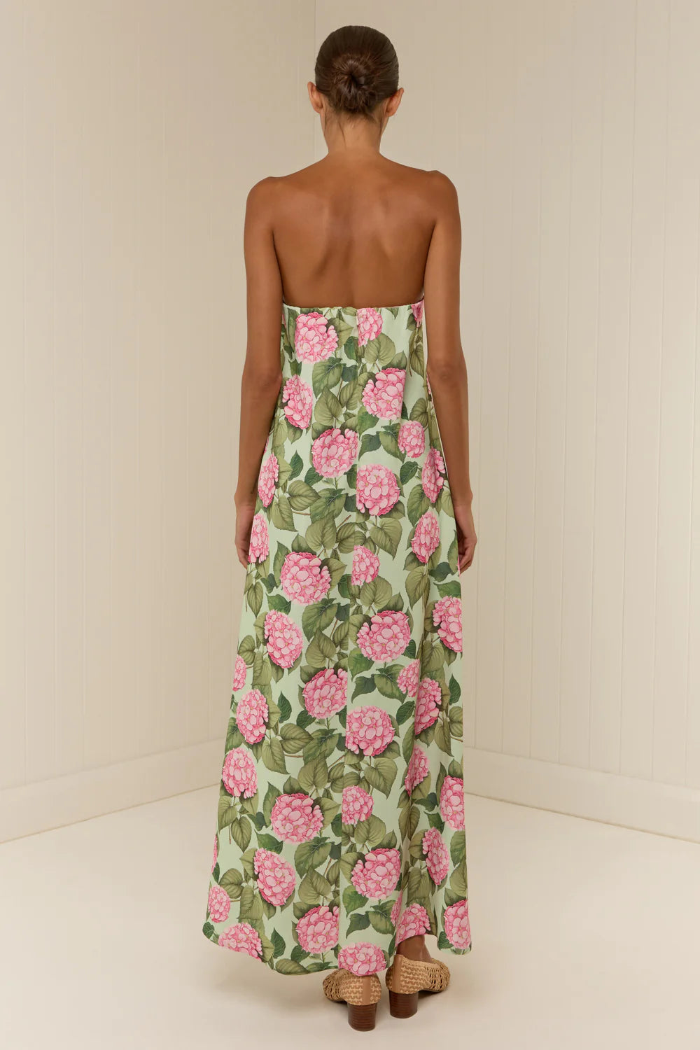 Woman wearing a strapless floral dress with pink flowers on a plain background