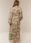 Woman wearing a long floral dress with pink flowers on a plain background