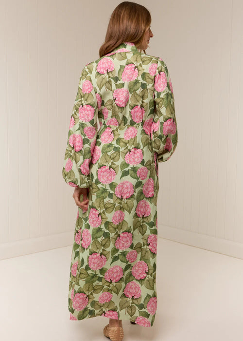 Woman wearing a long floral dress with pink flowers on a plain background