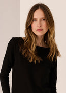 Woman wearing a black long-sleeve top  against a plain background