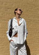 Person wearing a white outfit against a beige brick wall