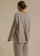 A woman modelling a matching two-piece loungewear set consisting of a long-sleeve knit top with a white collar and matching wide-leg pants, in a warm taupe-beige colour, set against a solid beige studio background.