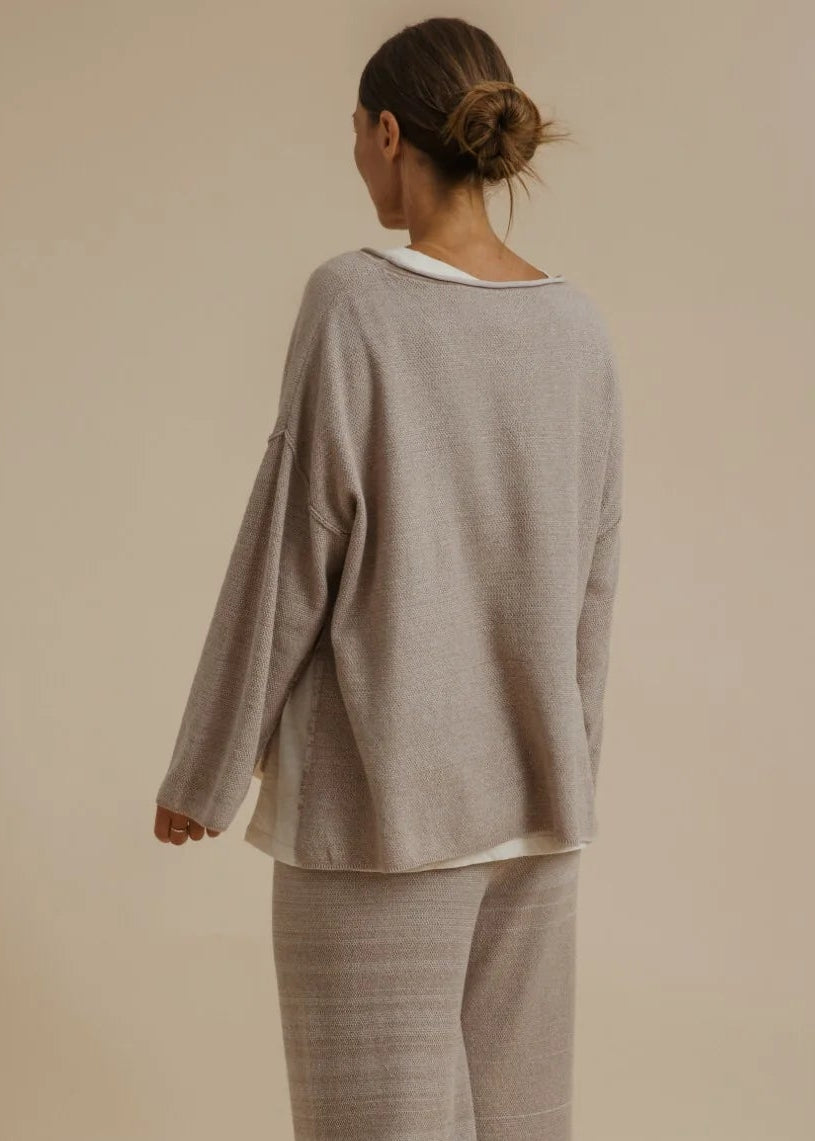 A woman modelling a matching two-piece loungewear set consisting of a long-sleeve knit top with a white collar and matching wide-leg pants, in a warm taupe-beige colour, set against a solid beige studio background.