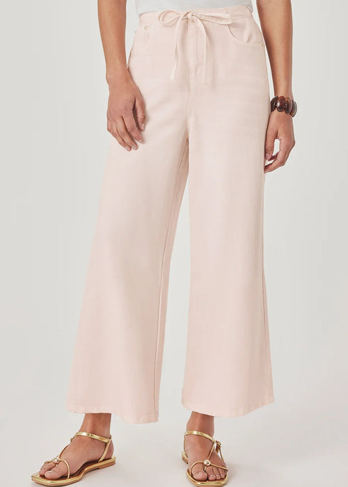 A model wearing light pink wide-leg cropped pants with a drawstring waist, paired with gold flat sandals, against a light grey studio background.