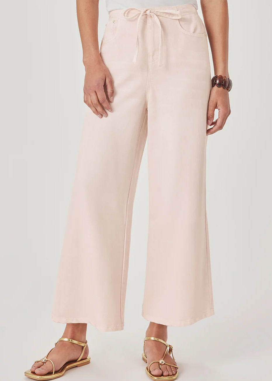 A model wearing light pink wide-leg cropped pants with a drawstring waist, paired with gold flat sandals, against a light grey studio background.