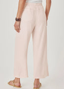 A model wearing light pink wide-leg cropped pants with a drawstring waist, paired with gold flat sandals, against a light grey studio background.