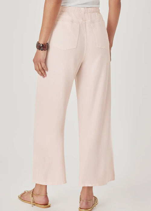 A model wearing light pink wide-leg cropped pants with a drawstring waist, paired with gold flat sandals, against a light grey studio background.